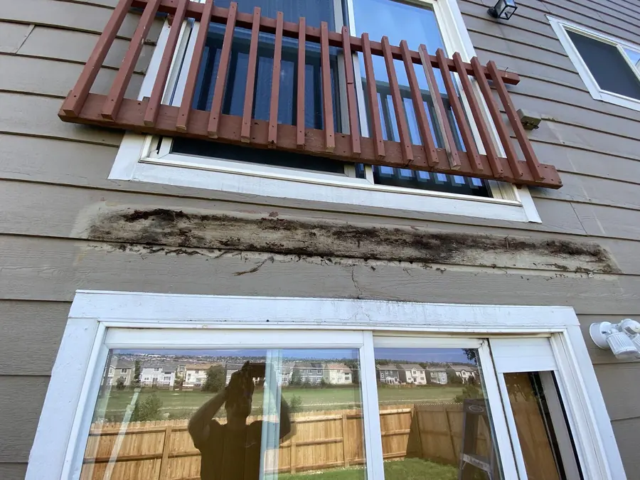 Siding and trim below an old deck, stained and rotted along the ledger line