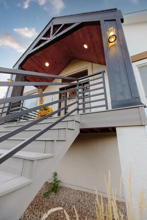 Modern horizontal railing on stairs beneath a cedar-clad porch roof at dusk