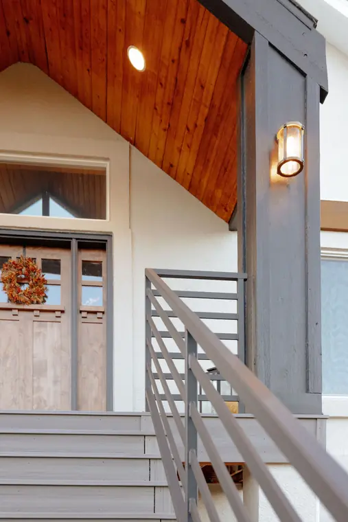 Modern horizontal railing on a covered front entry, beside the door under a cedar ceiling