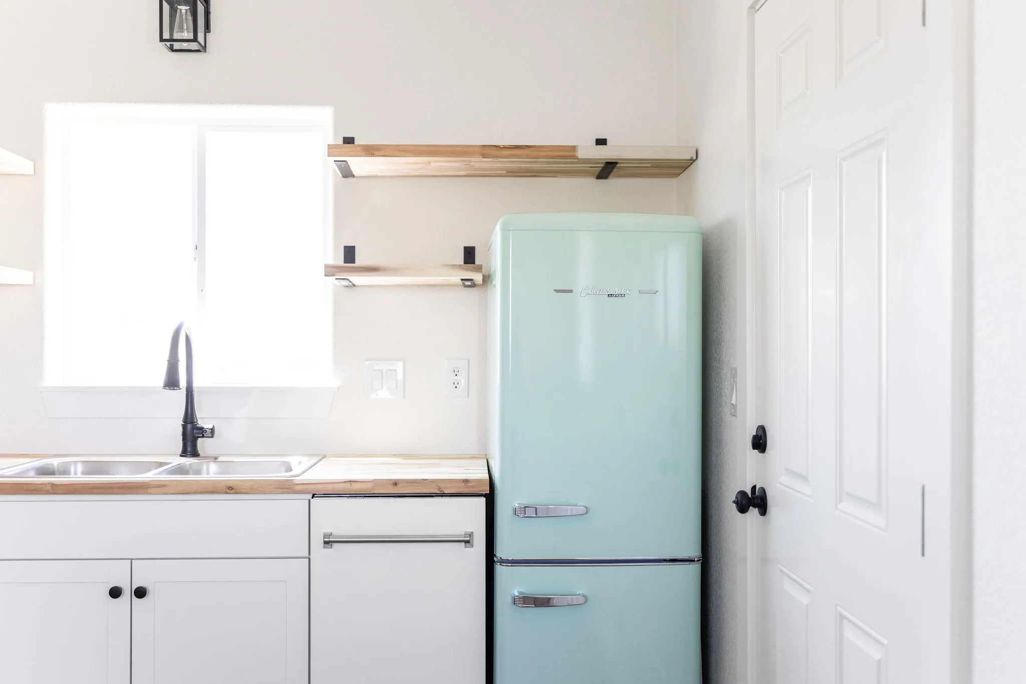 A tiny-home kitchen with white cabinets, butcher-block counters, open shelves and a mint retro fridge