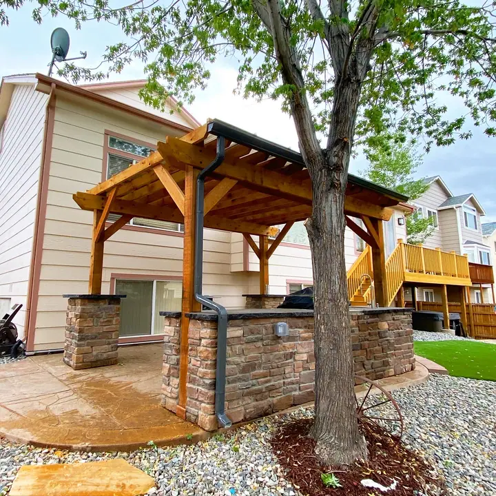 A cedar pergola with a clear SkyPoly roof over a stone outdoor kitchen