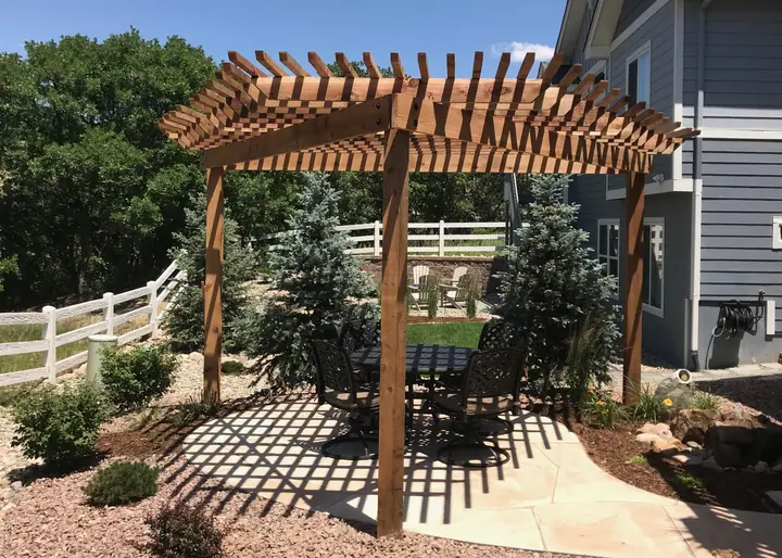 A cedar pergola casting striped shade across a patio and garden