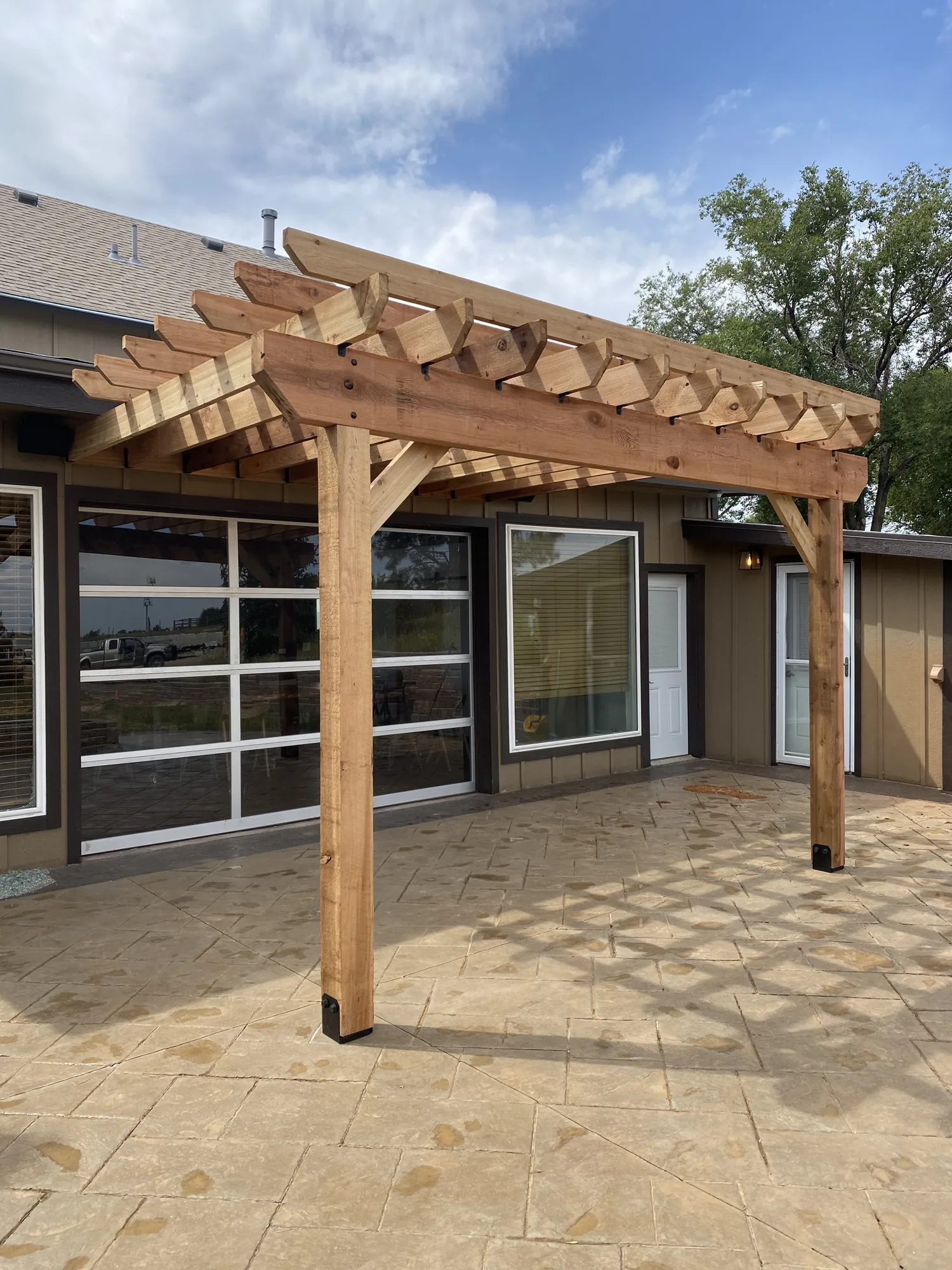 An attached cedar pergola over a stamped concrete patio beside a glass garage door