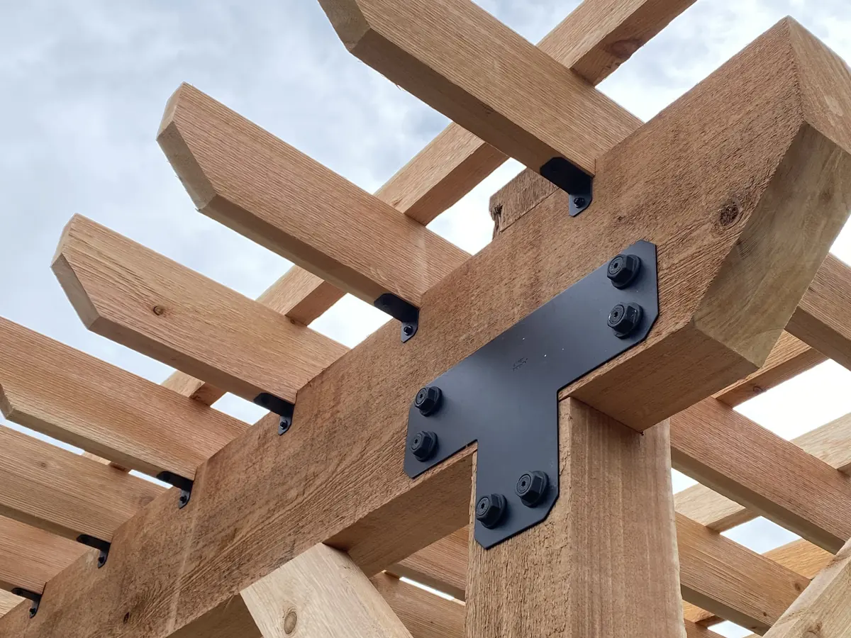 A black steel bracket joining cedar beams and rafters at a post