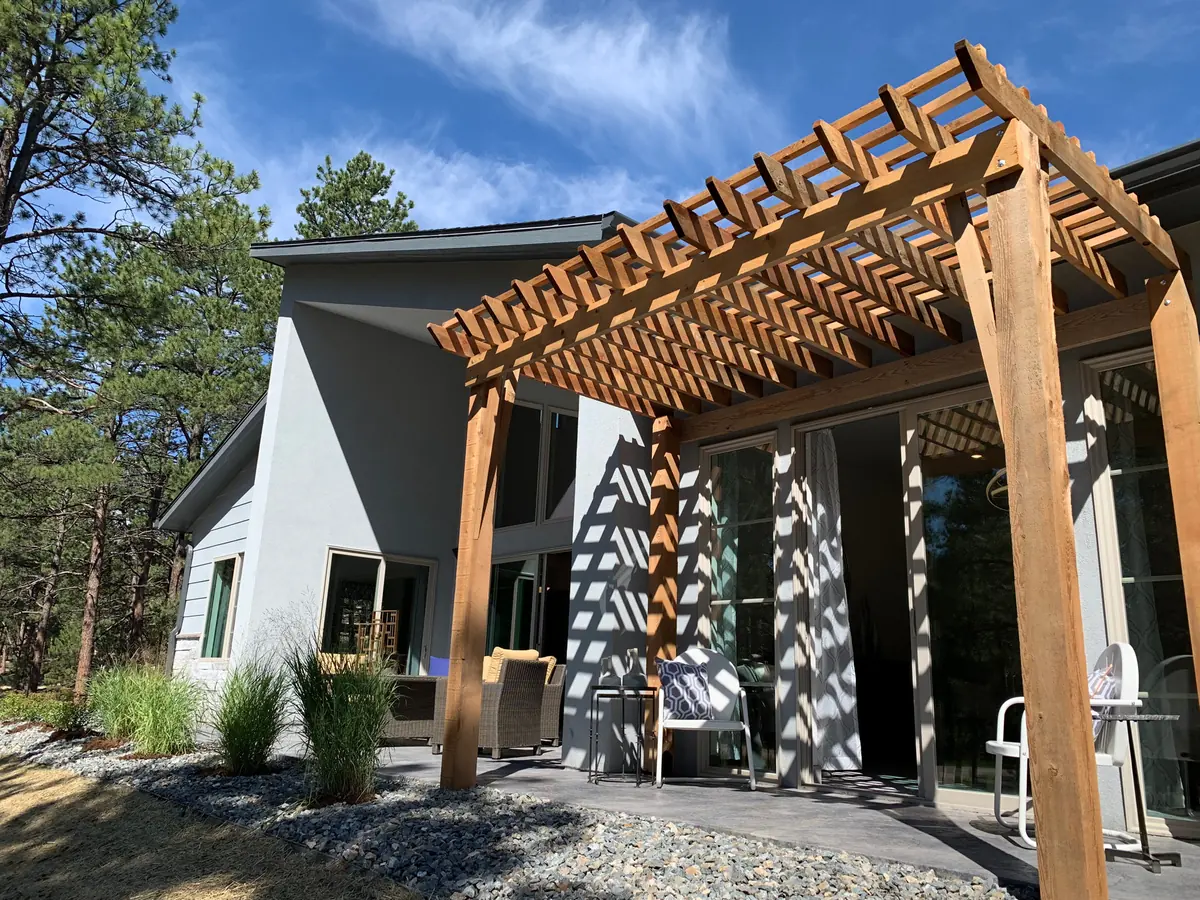 A cedar pergola over a patio at the back of a modern house