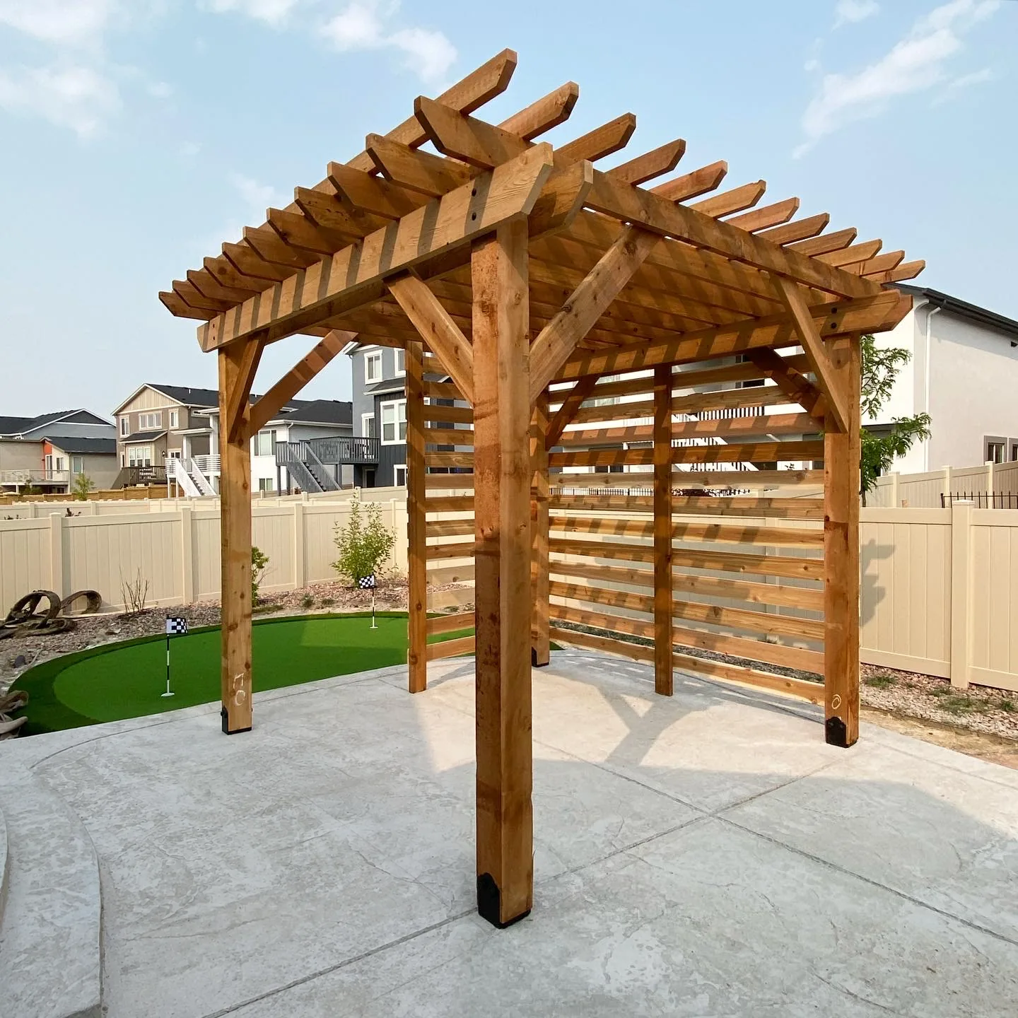 A detached cedar pergola with a slatted privacy wall beside a putting green