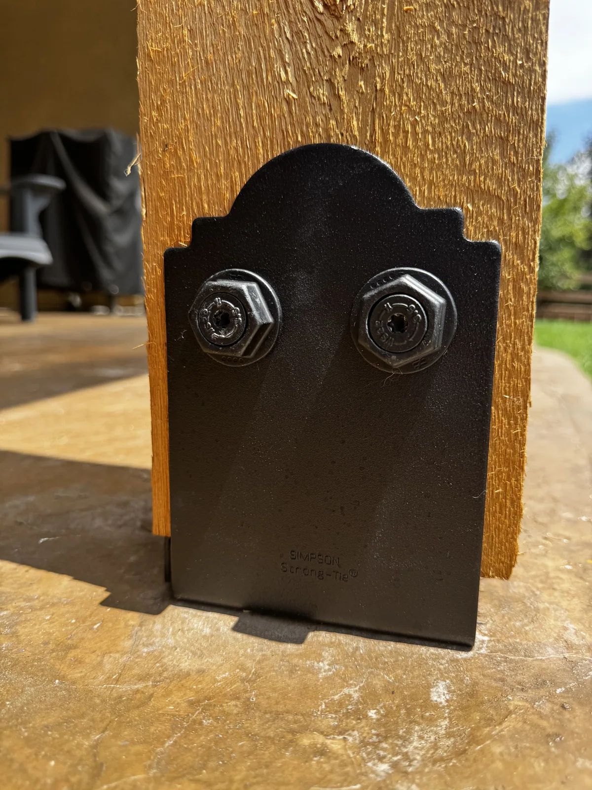 A black Simpson post base bolted to a cedar post and anchored to the concrete slab