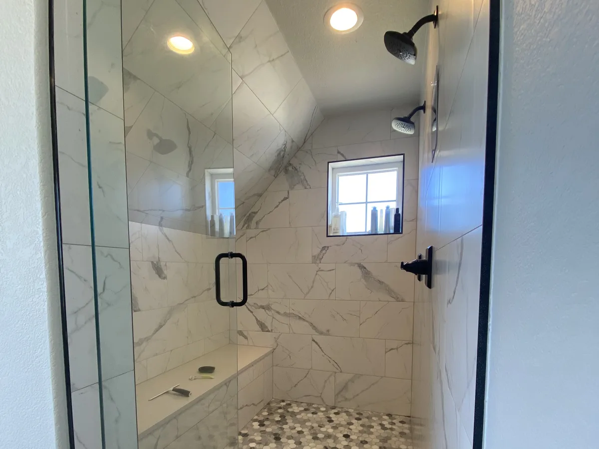 A remodelled walk-in shower with two shower heads, marble tile and a hexagon mosaic floor