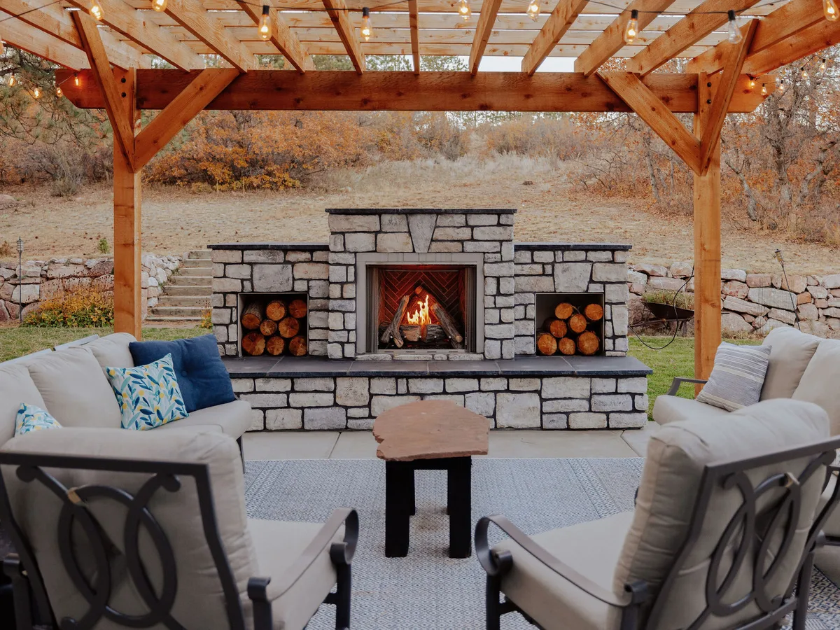 A stone outdoor fireplace and seating under a cedar pergola at Winding Oaks